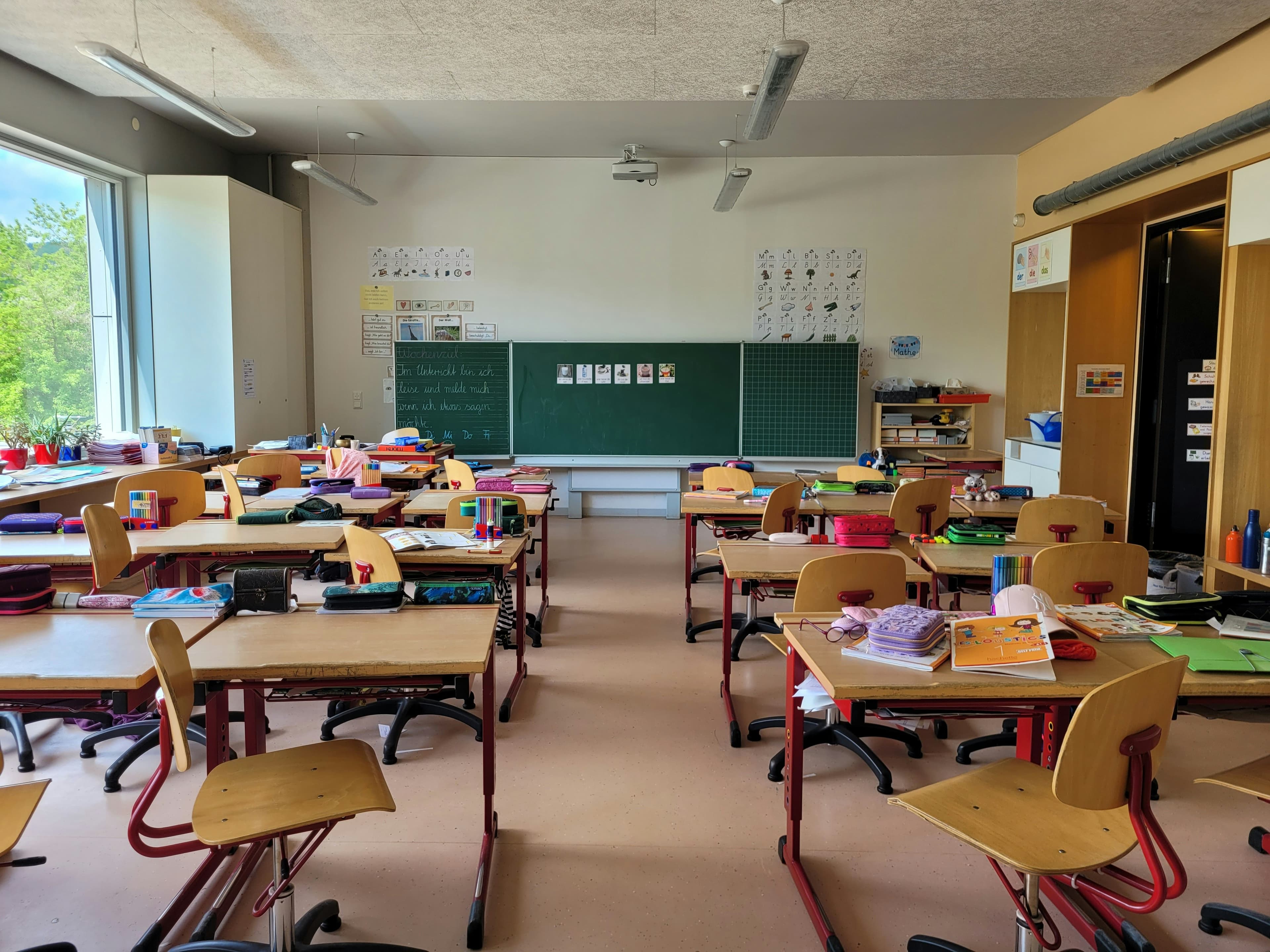 A primary school classroom with desks, supplies and a green chalkboard