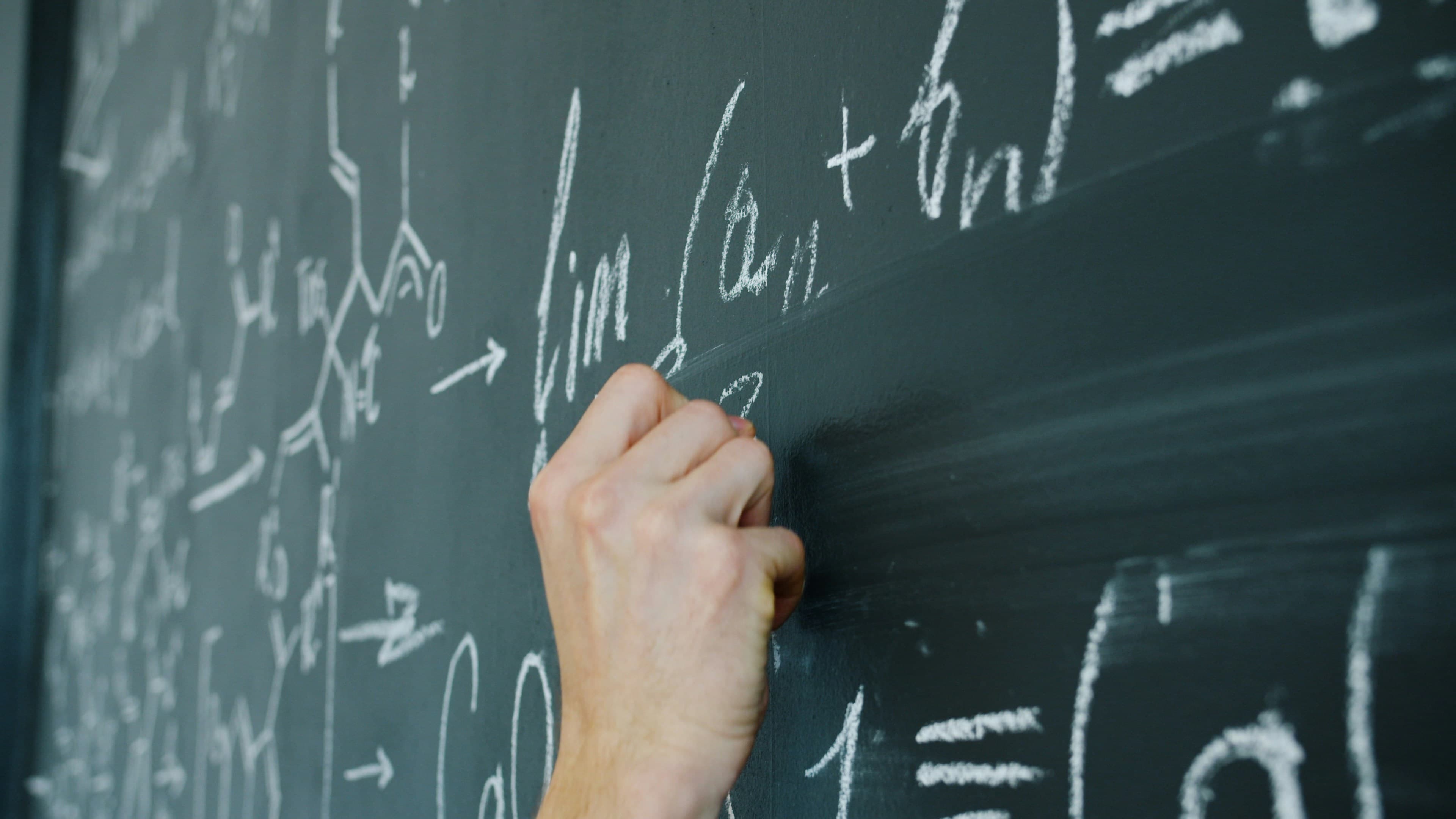 A hand writing calculus formulas in chalk on a blackboard