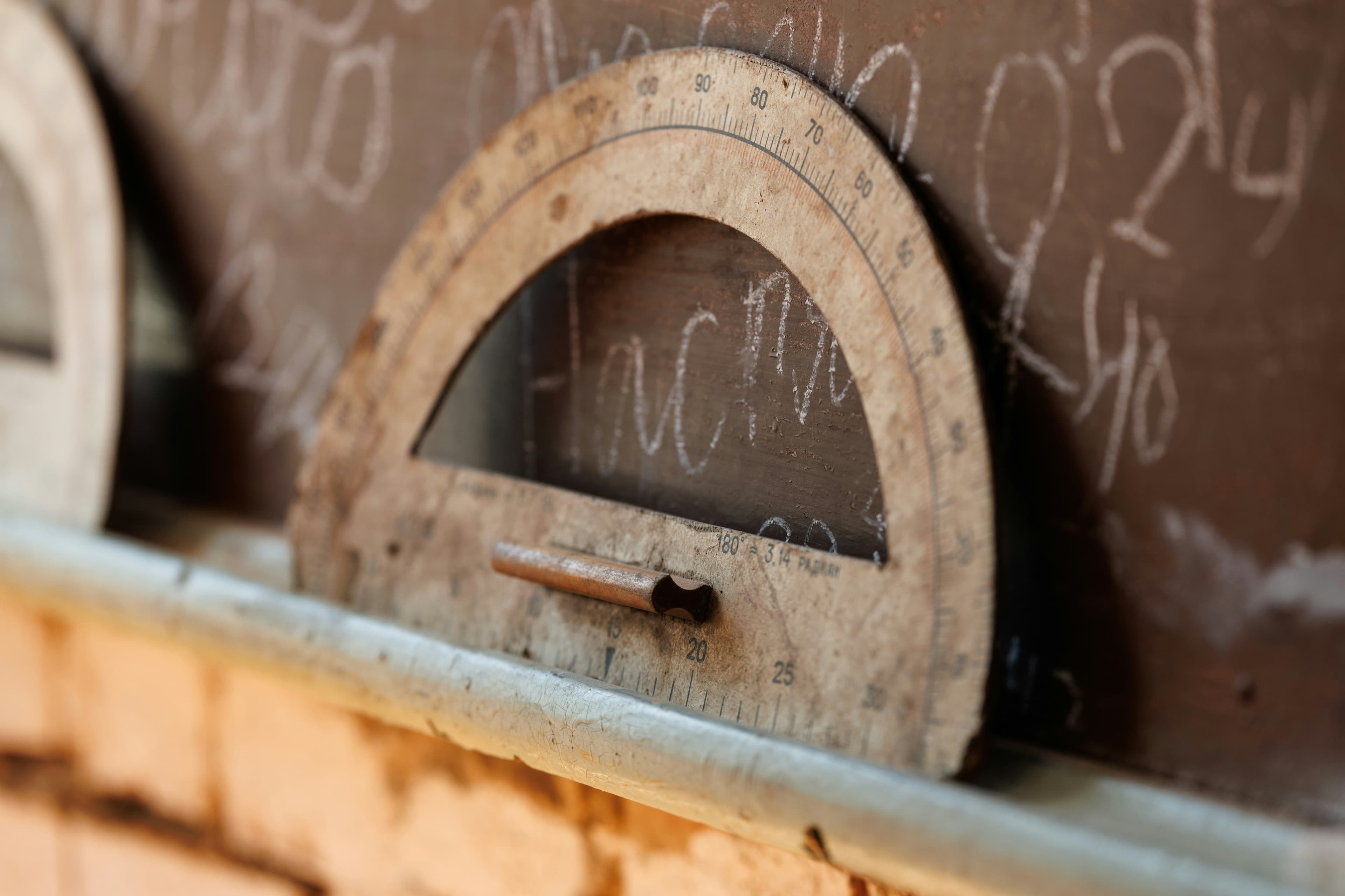 A wooden protractor resting on a chalkboard ledge